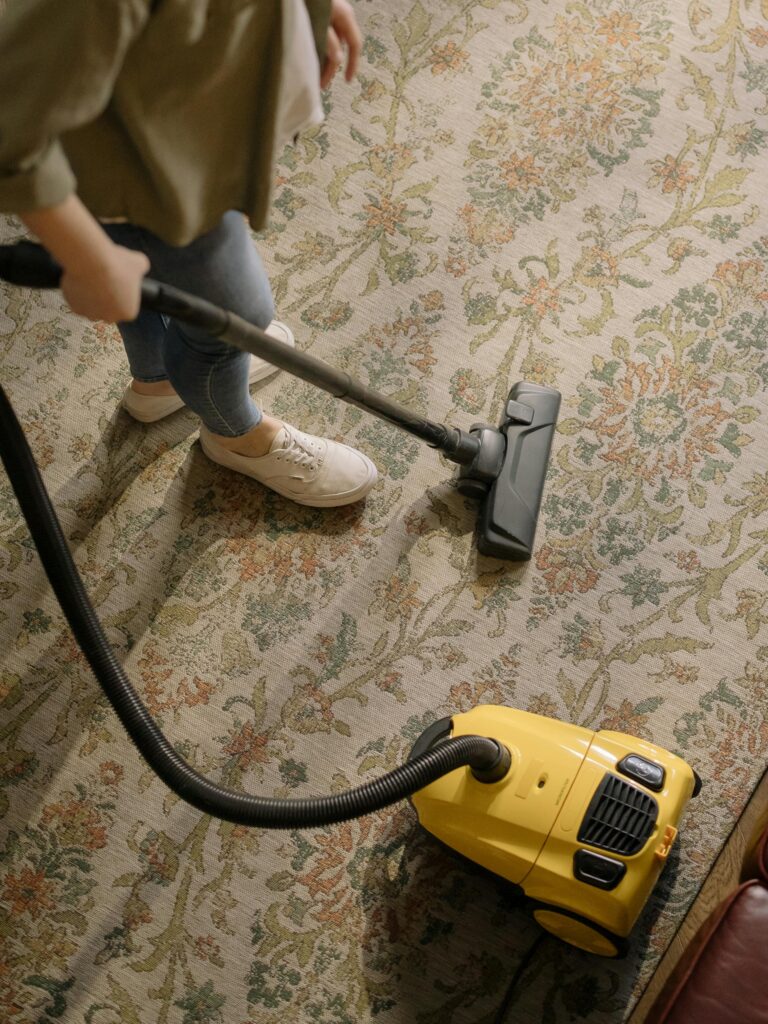 Person cleaning a floral carpet with a yellow vacuum cleaner indoors.